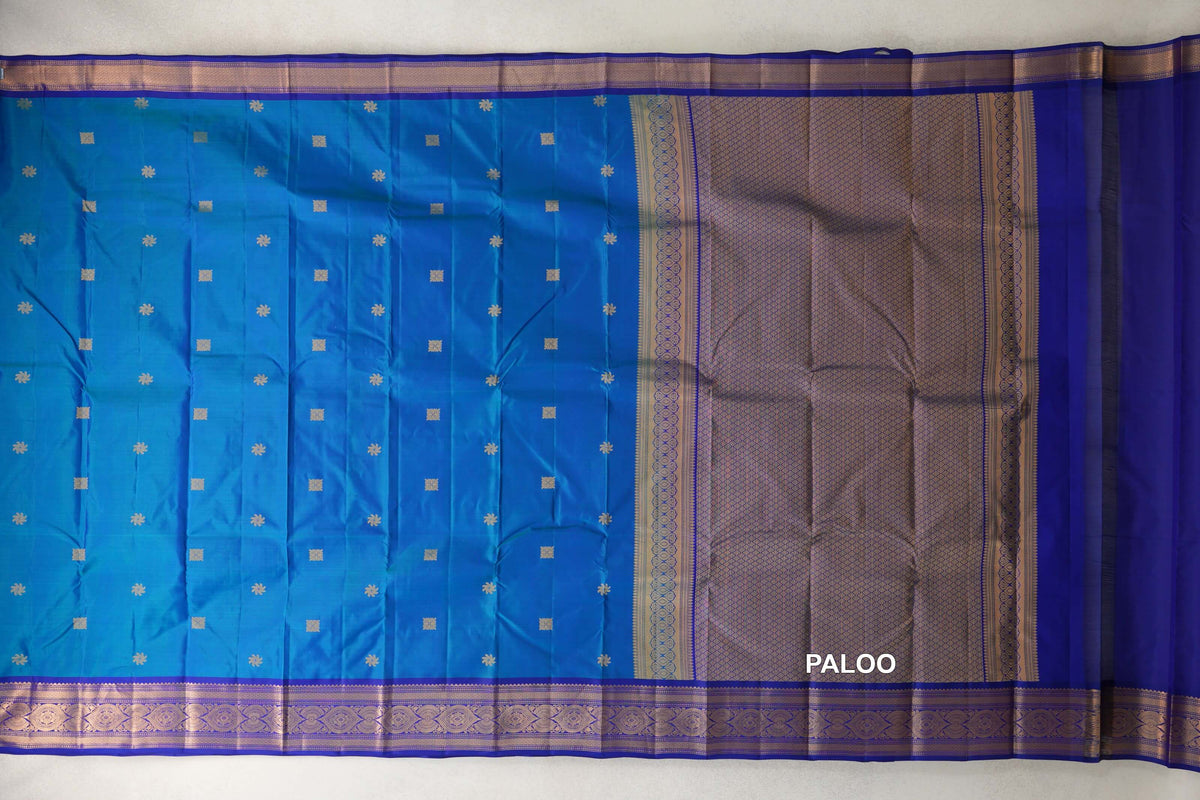 Light weight Kanchipuram silk saree spread out, with a peacock blue body, small gold motifs, deep royal blue borders and a lattice-patterned pallu.