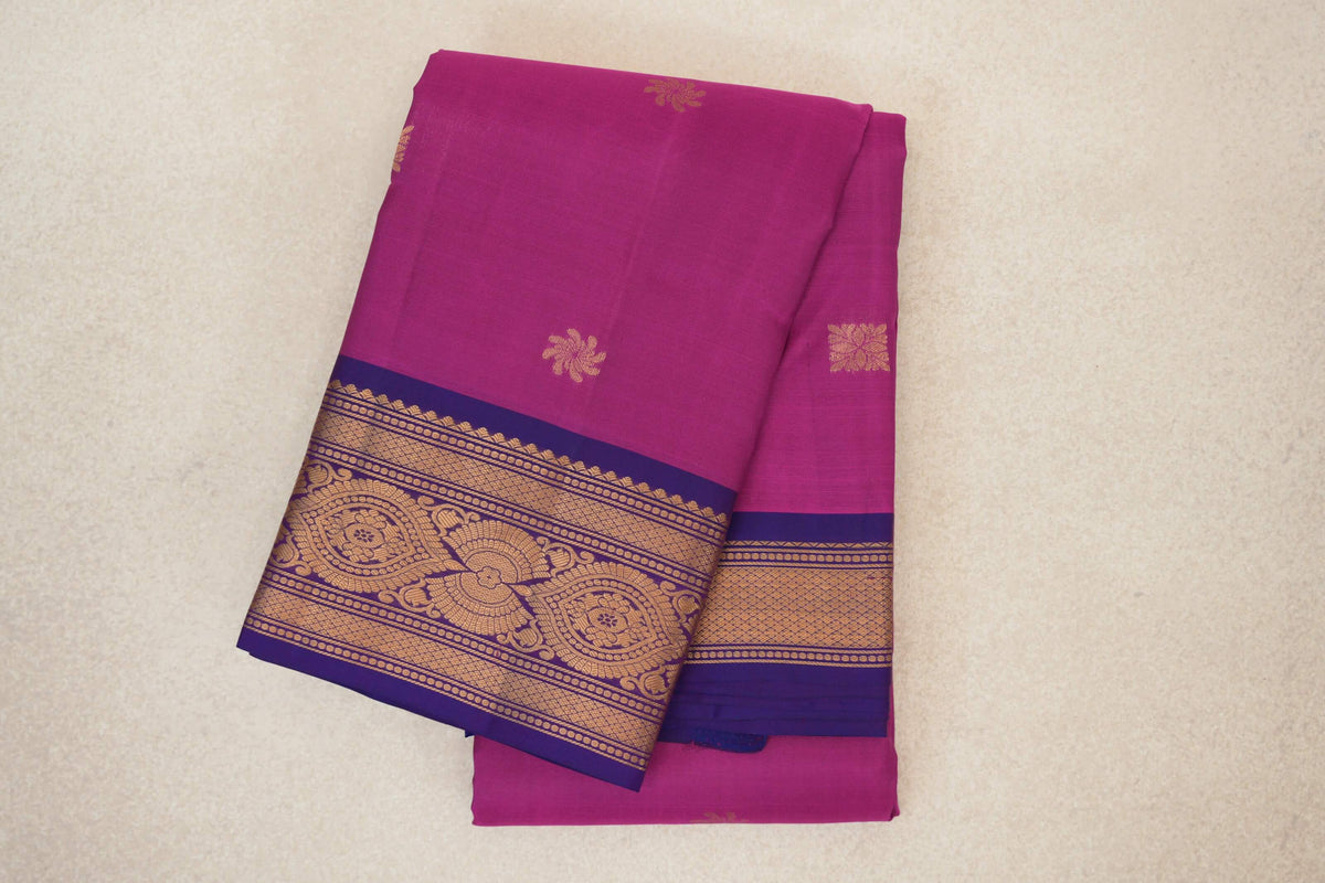 Folded deep magenta lightweight Kanchipuram silk saree with small gold motifs and ornate gold-patterned violet purple borders.