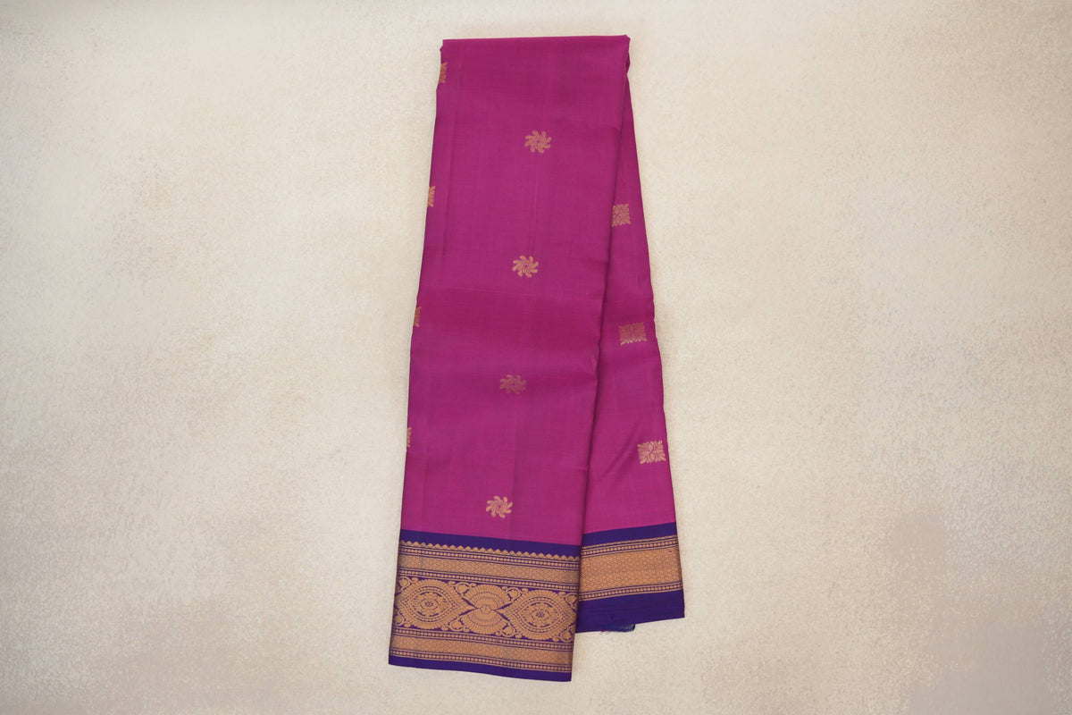 Folded deep magenta lightweight Kanchipuram silk saree with scattered gold floral motifs and a violet purple border woven with gold patterns.