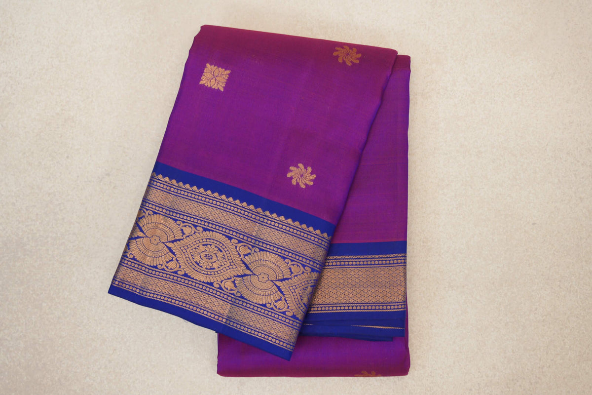 Folded light weight Kanchipuram silk saree in rani pink with scattered gold floral motifs and deep royal blue borders patterned in gold.