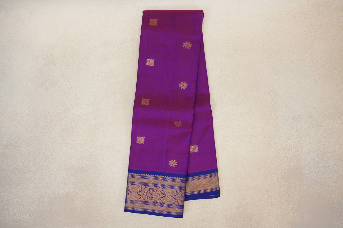 Folded lightweight Kanchipuram silk saree with a rani pink body, scattered gold floral motifs and a deep royal blue border with gold patterns.