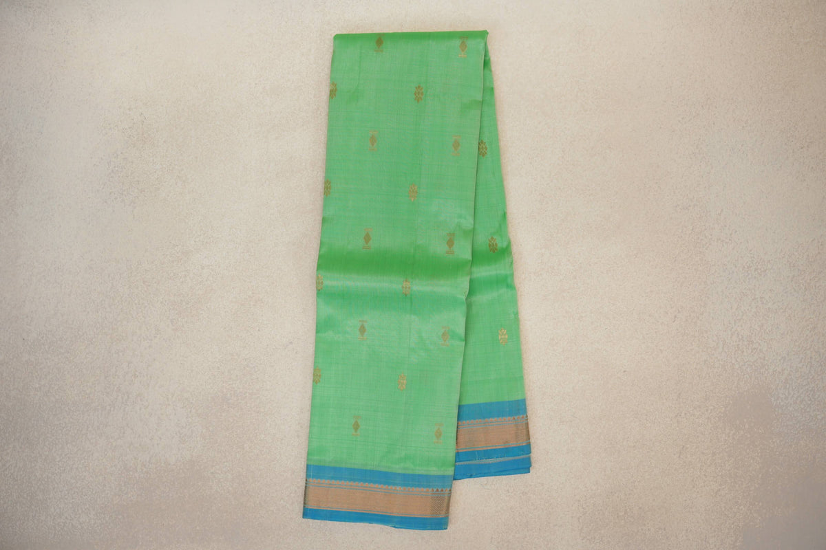 Folded mint green lightweight Kanchipuram silk saree with scattered gold motifs and a light turquoise blue border with gold detailing.