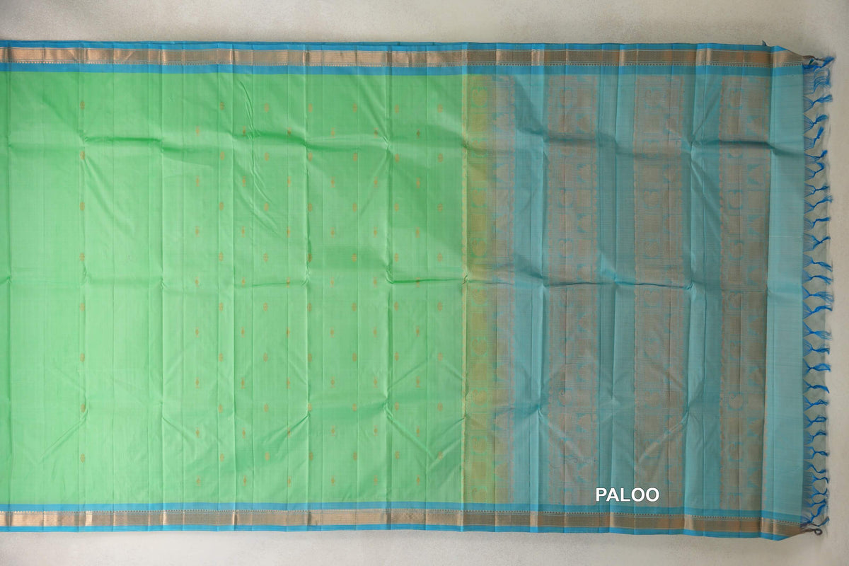 Kanchipuram silk saree spread flat, with a mint green body, small gold motifs, light turquoise blue borders and a patterned pallu with blue tassels.