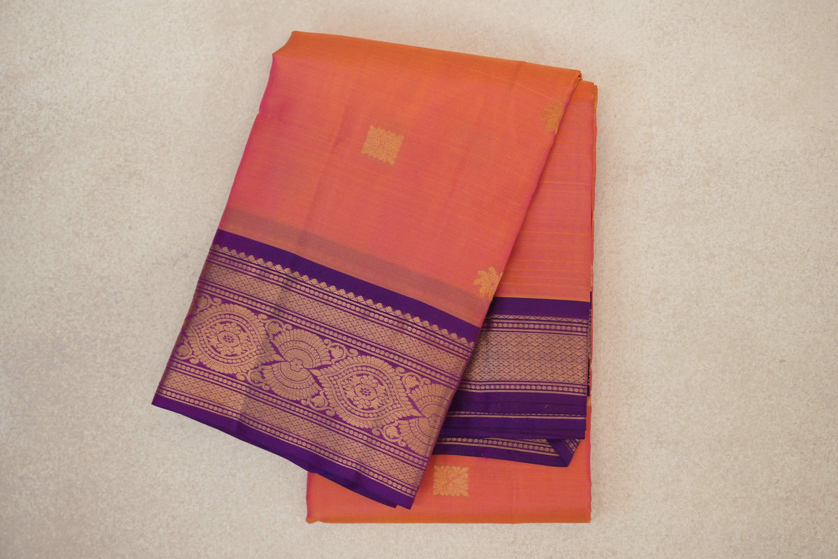 Folded light weight Kanchipuram silk saree in pink and yellow, with small gold-toned accents and an ornate violet purple border.