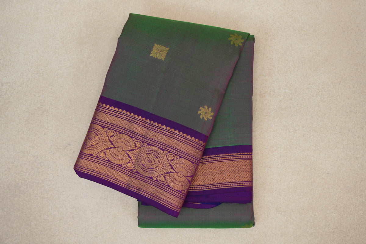Folded lightweight Kanchipuram silk saree with a green body, small gold motifs and a violet purple border woven with intricate gold patterns.