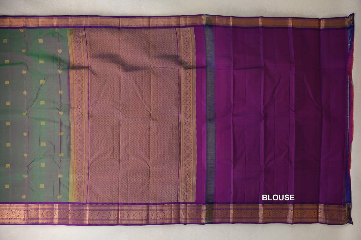 Kanchipuram silk saree spread out, showing a green body with small gold motifs, a patterned violet purple pallu, ornate borders and a matching blouse piece.