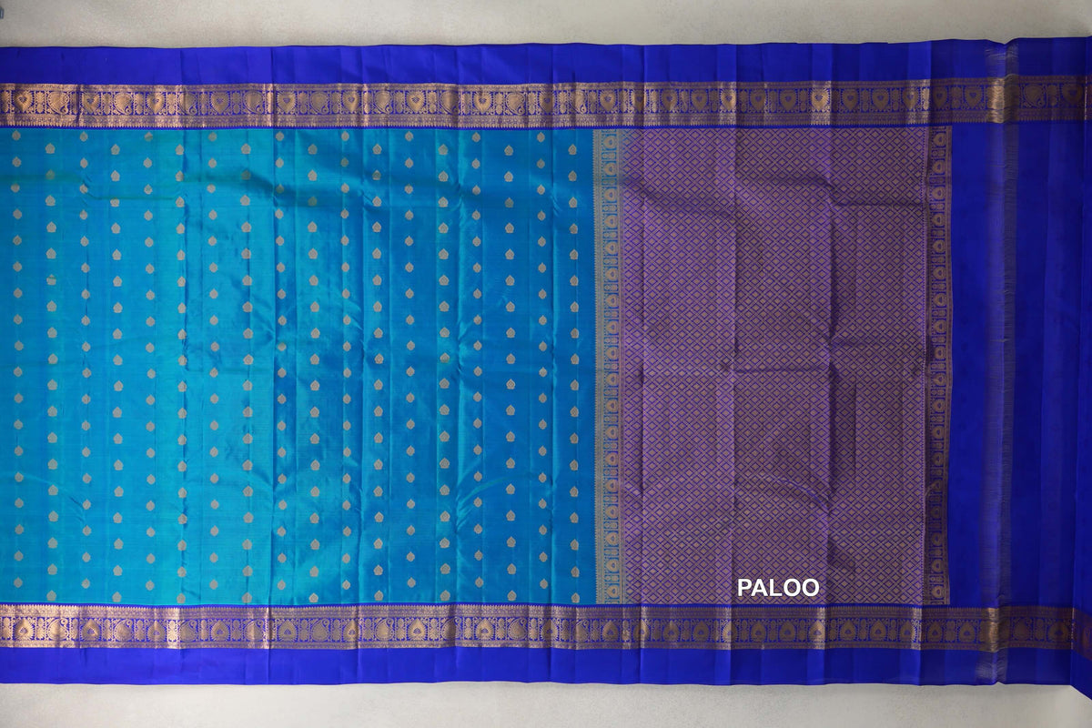 Light Weight Kanchipuram silk saree spread out, with a peacock blue body dotted with gold motifs, royal blue borders and a lattice-patterned pallu.