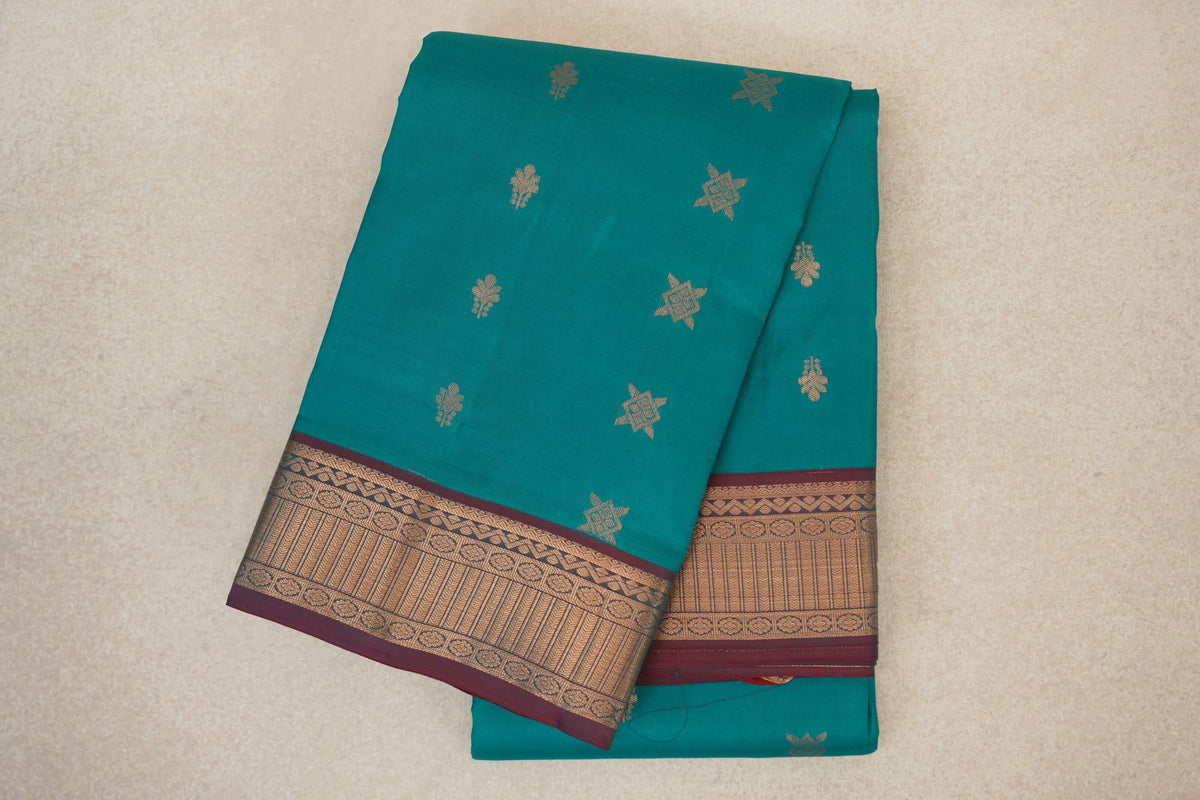Folded peacock green Kanchipuram silk saree with scattered gold-toned motifs and a patterned gold border edged in maroon.