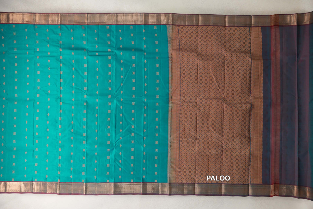 Peacock green Kanchipuram silk saree spread flat, with small gold-toned motifs, patterned maroon borders and a diamond-patterned pallu.