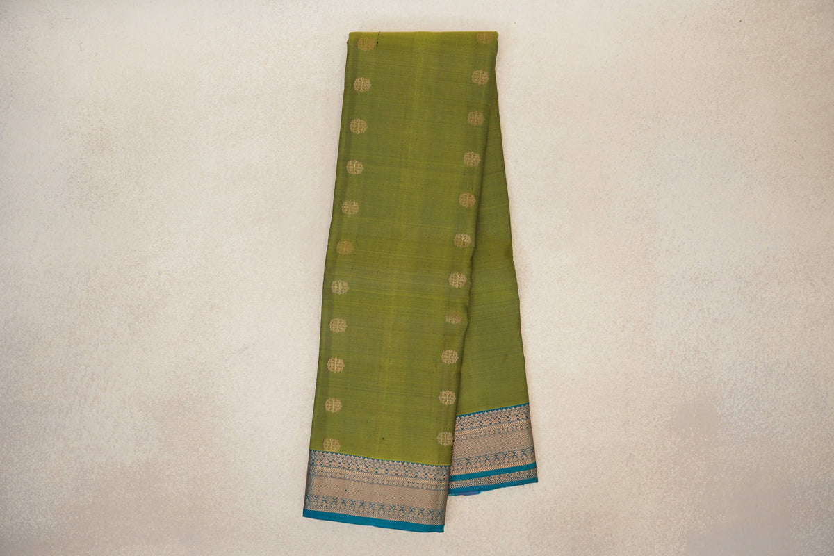 Folded olive green lightweight Kanchipuram silk saree with small gold-toned round motifs and a patterned teal blue border.