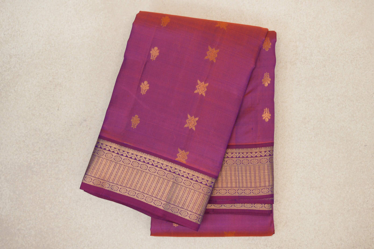 Folded blue and red Kanchipuram silk saree with a purple-toned body, scattered gold-coloured motifs and a broad patterned border.