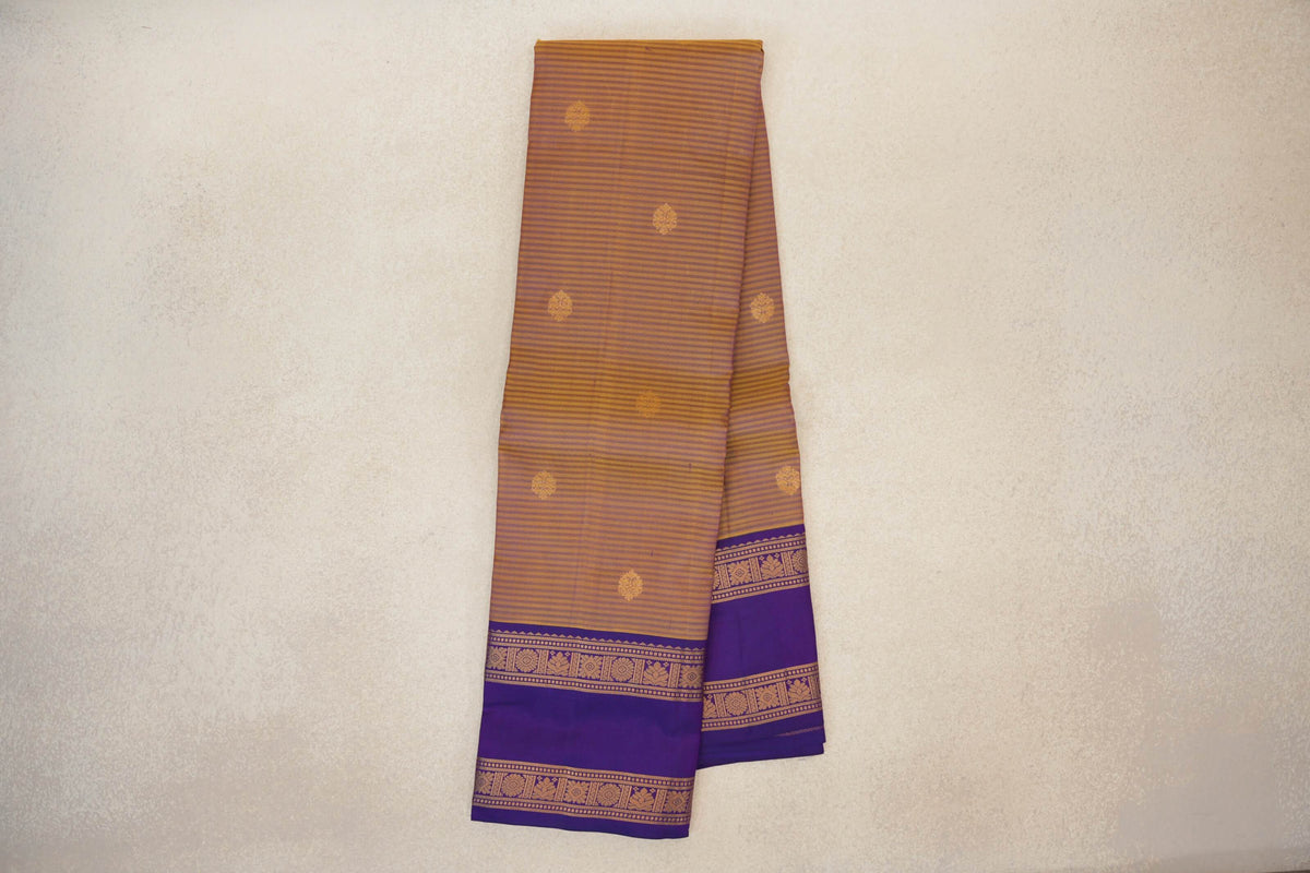 Folded mustard yellow Kanchipuram silk saree with fine stripes, scattered gold motifs and deep purple borders with patterned gold bands.