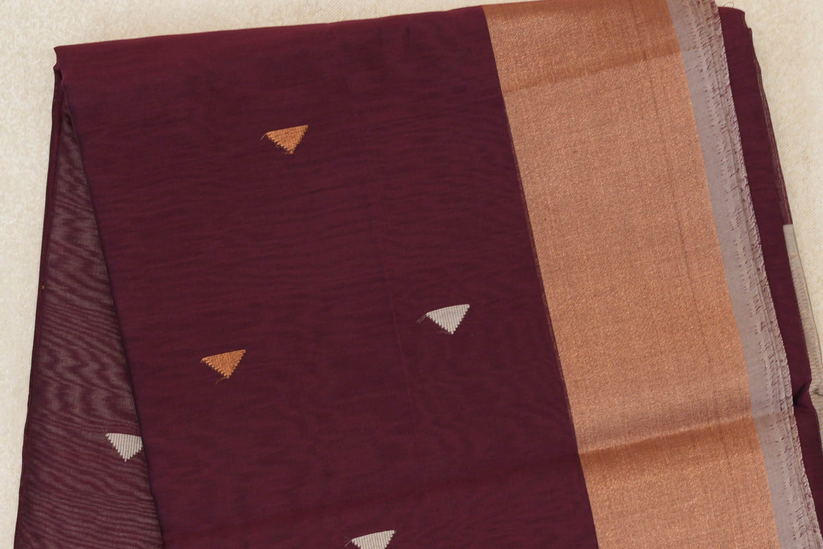 Folded Maheshwari silk cotton saree showing a deep wine maroon body with small triangular motifs, a broad copper-toned band and silver grey selvedge.