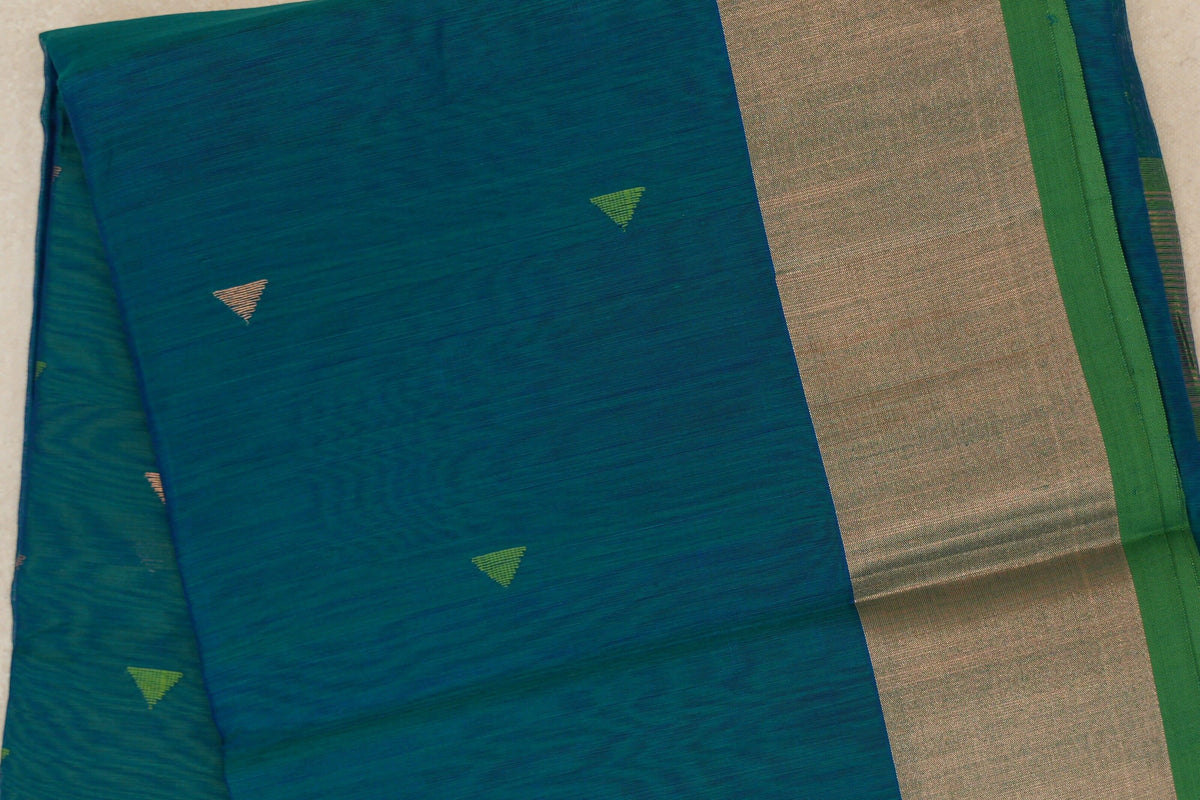 Close-up of a folded peacock blue Maheshwari silk cotton saree with small green and pale triangular motifs, a broad silvery band and parrot green edge.