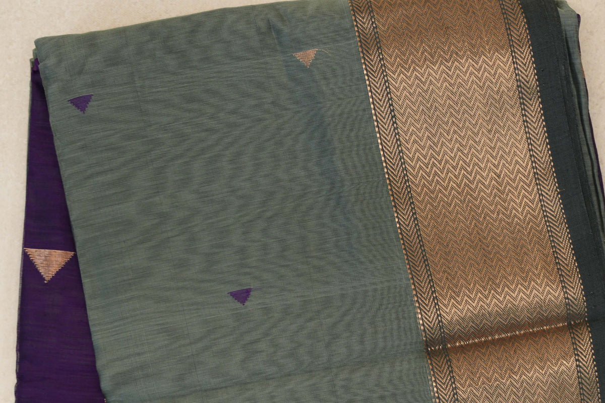 Folded Maheshwari silk cotton saree with a sage green body, small purple triangles, a wide copper-toned chevron border and deep purple fabric beneath.