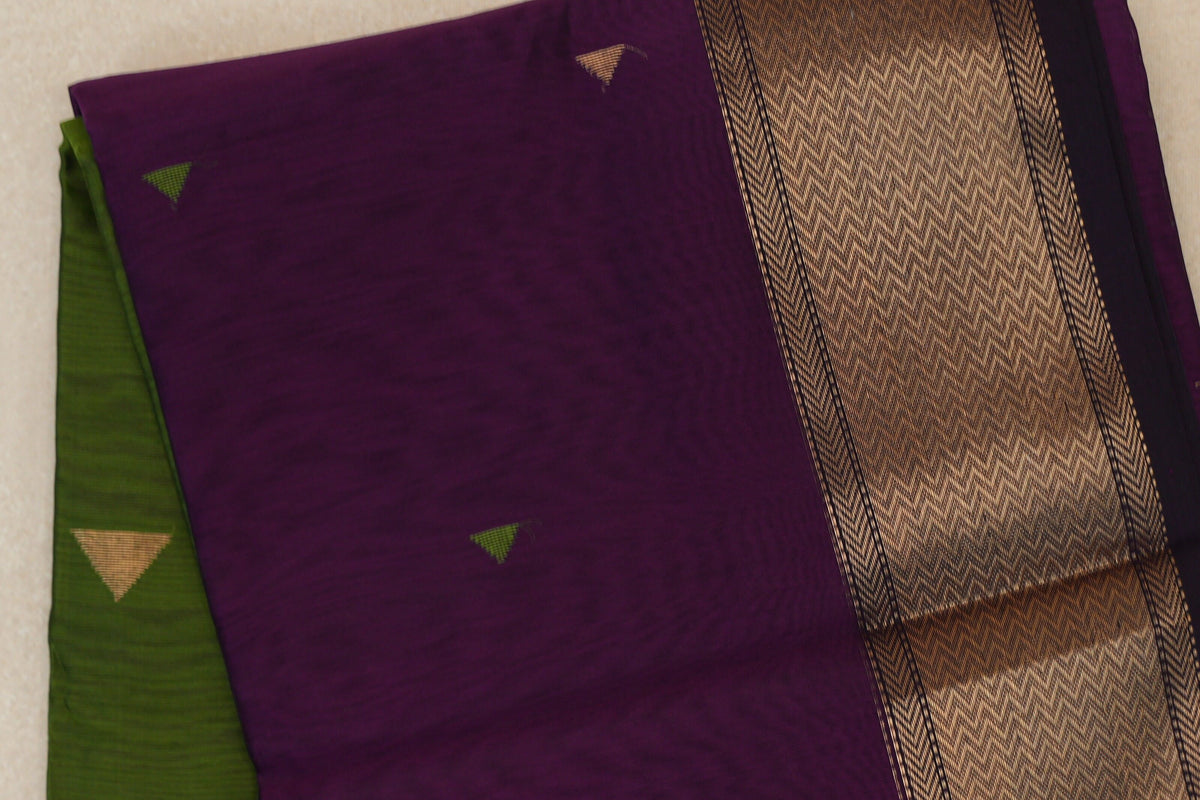 Folded deep purple Maheshwari silk cotton saree with small triangle motifs, a broad patterned gold border and an olive green section at the side.
