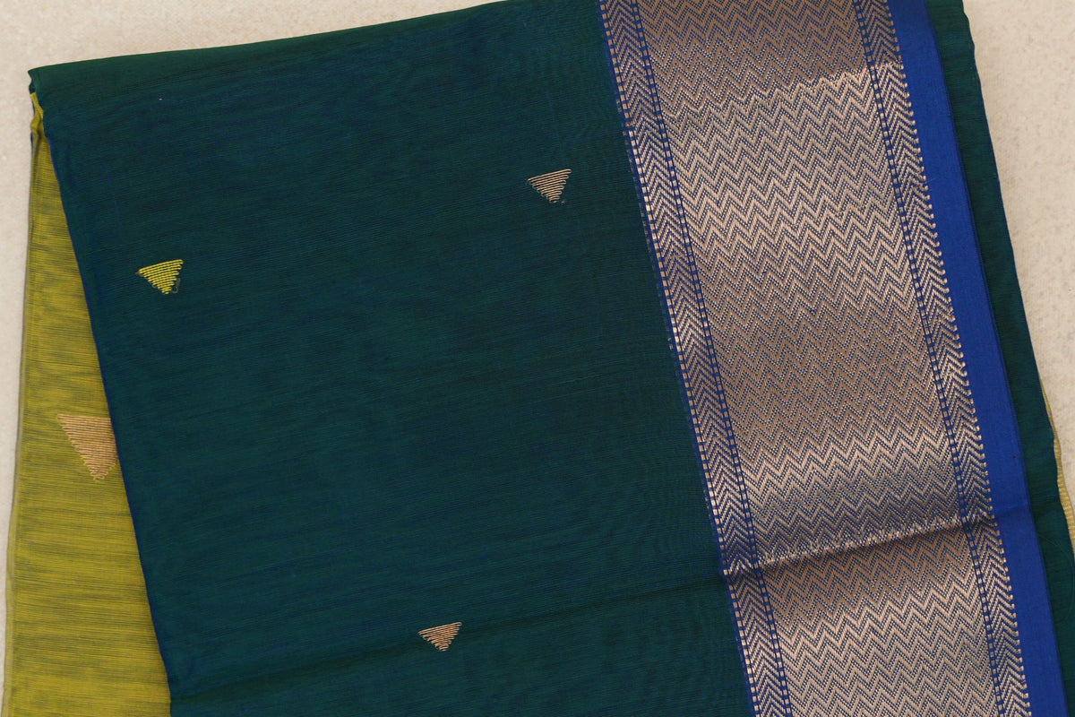 Folded Maheshwari silk cotton saree showing a peacock green body with small gold triangles and a royal blue border with a metallic chevron pattern.