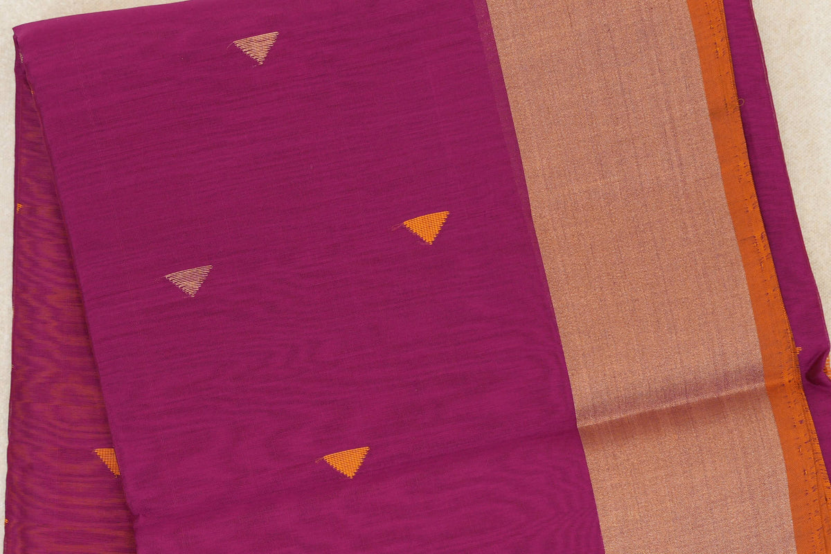 Folded Maheshwari silk cotton saree in deep magenta, with small orange triangular motifs, a broad gold-toned border and orange selvedge.