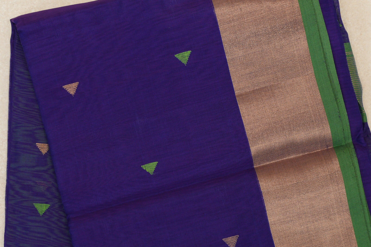 Folded close-up of a deep violet Maheshwari silk cotton saree with small green and gold triangles, a broad gold-toned border and green selvedge.