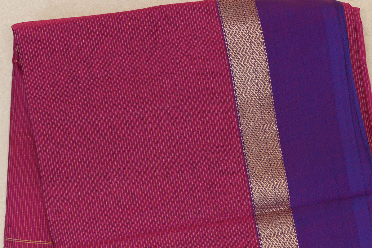Folded Maheshwari silk cotton saree with a finely striped deep rani pink body, a metallic zigzag band and a wide violet purple border.