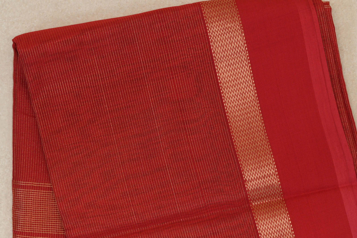 Folded red Maheshwari silk cotton saree with fine gold-toned stripes, a zigzag-patterned border and a plain red panel.