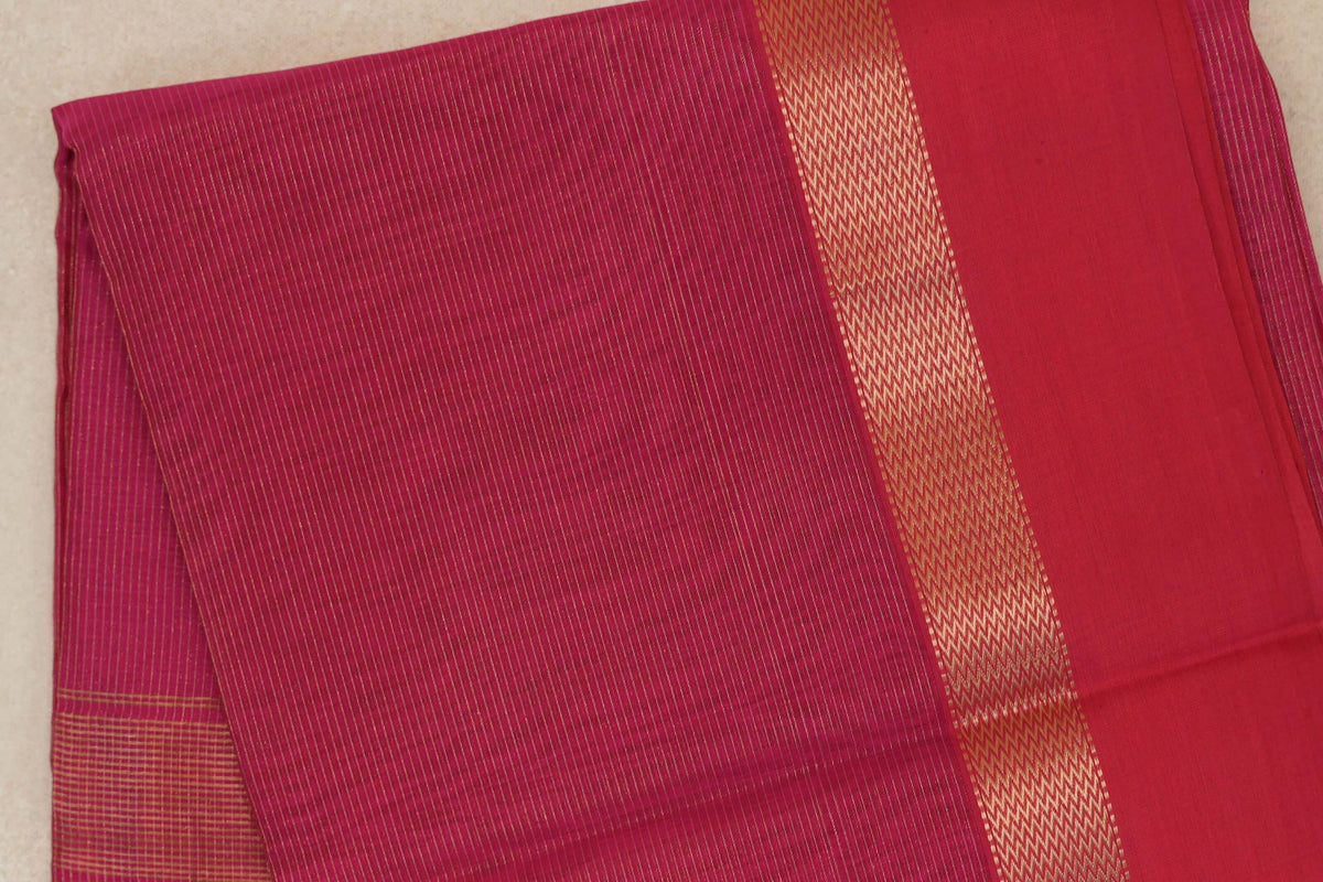 Folded rani pink Maheshwari silk cotton saree with fine gold pinstripes, a broad patterned gold band and a plain pink section.