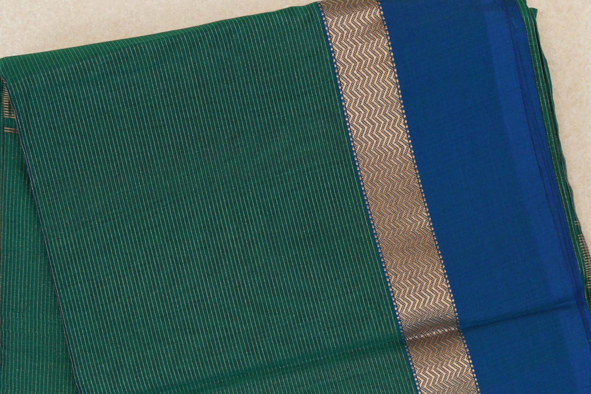 Folded Maheshwari silk cotton saree showing a finely striped bottle green body, gold zigzag band and broad peacock blue border.