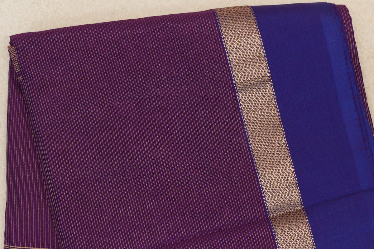 Folded Maheshwari silk cotton saree showing a deep purple body, a violet purple section with fine gold stripes, and a gold zigzag band.