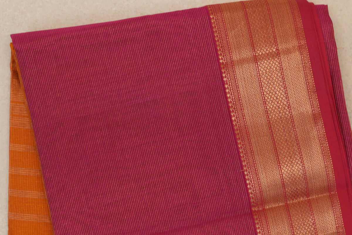 Folded rani pink Maheshwari silk cotton saree with fine gold stripes, a wide patterned gold border and orange fabric peeking out beneath.