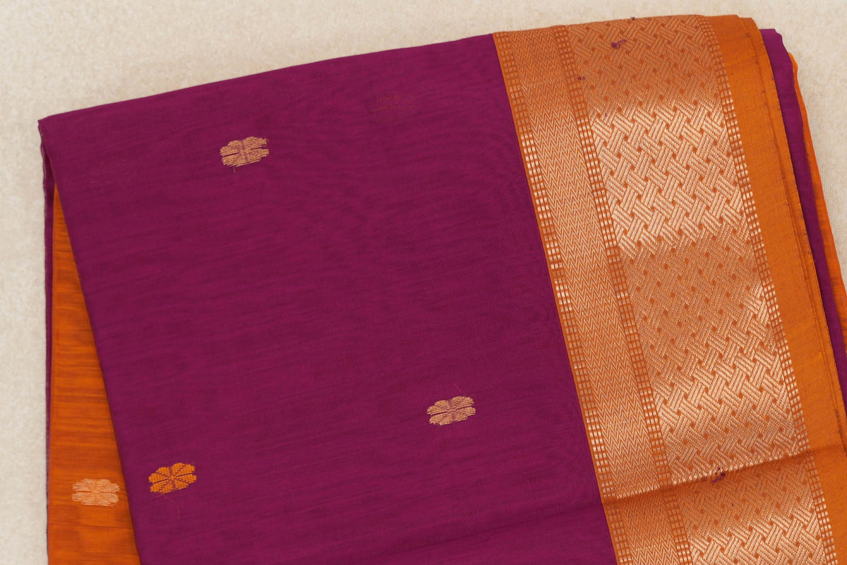 Folded Maheshwari silk cotton saree with a dark magenta body, small gold motifs and a deep orange border with metallic geometric patterns.