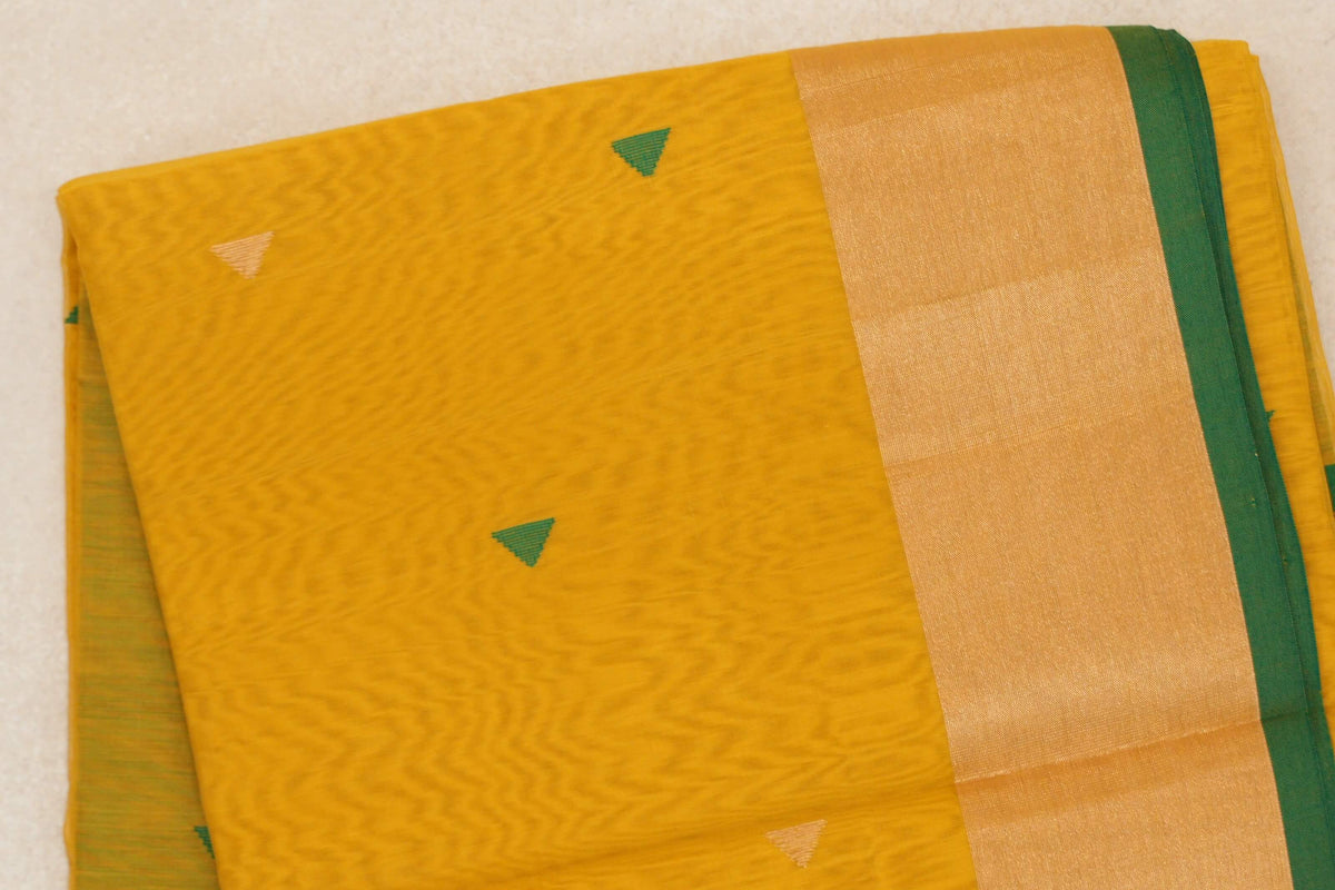 Folded turmeric yellow Maheshwari silk cotton saree with small green and pale gold triangles, a broad glossy border and bottle green selvedge.