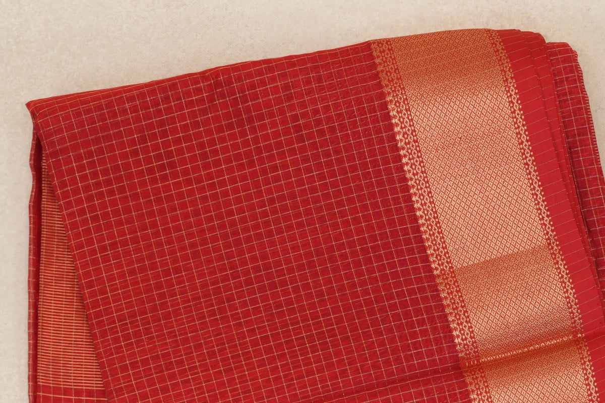 Folded tomato red Maheshwari silk cotton saree with fine gold checks and a broad gold zari border edged in red.