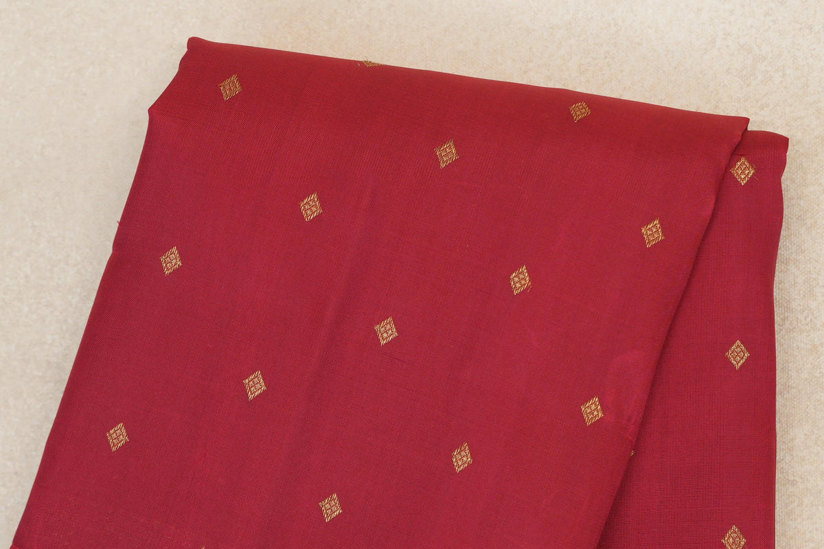 Folded crimson red heirloom Kanjivaram silk saree showing the body with scattered small gold-coloured diamond motifs.