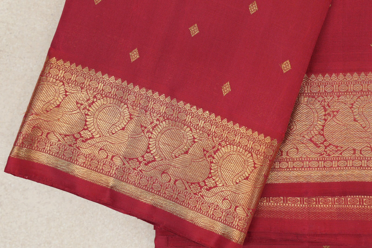 Close-up of folded crimson red heirloom Kanjivaram silk saree with small gold-toned diamond motifs and an ornate paisley border.