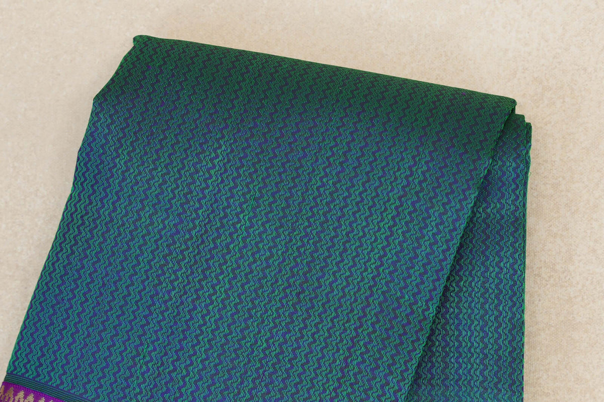 Folded peacock green Kanjivaram silk saree with a dense purple geometric pattern and a glimpse of the purple border.