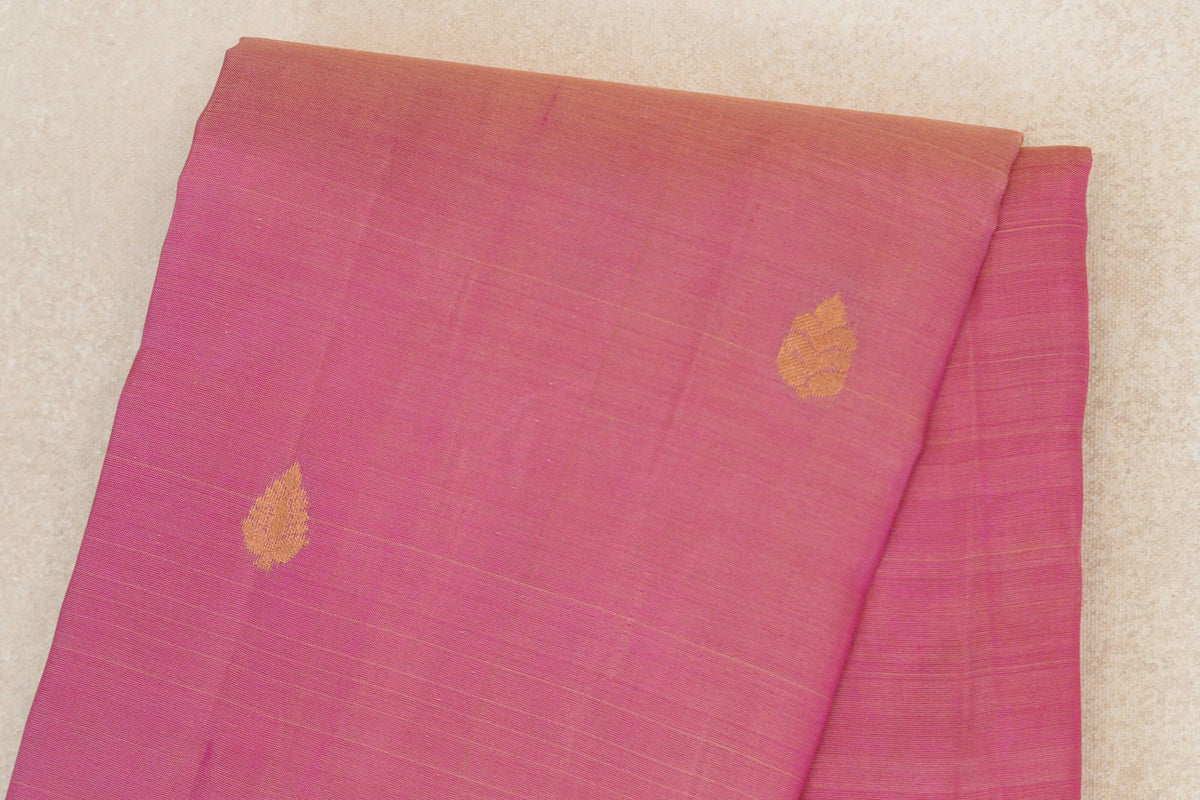 Close-up of folded rose pink Kanchipuram silk saree fabric with small gold leaf-shaped motifs and fine horizontal weave lines.