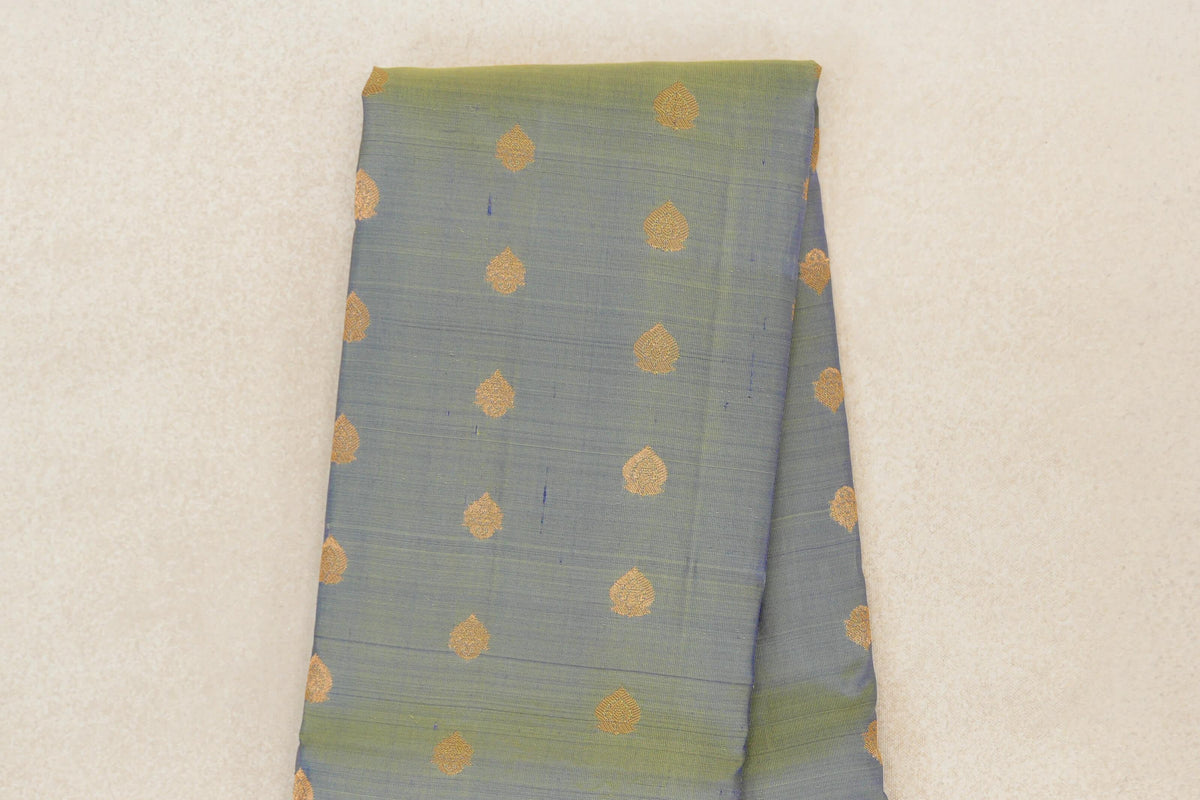 Folded yellowish green lightweight Kanchipuram silk saree body with spaced gold motifs and fine horizontal weave lines.