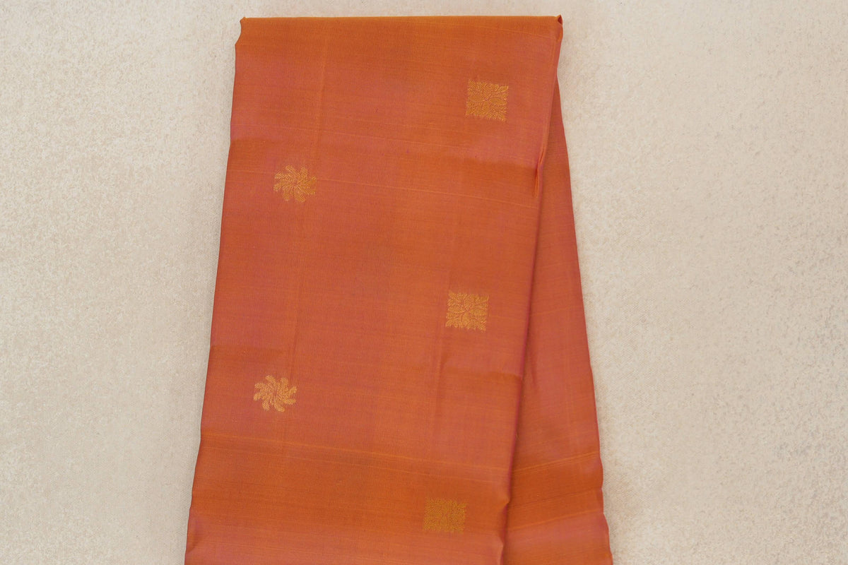 Folded Kanchipuram silk saree body in pink and yellow, appearing coral, with scattered gold-toned floral and geometric motifs and fine horizontal lines.