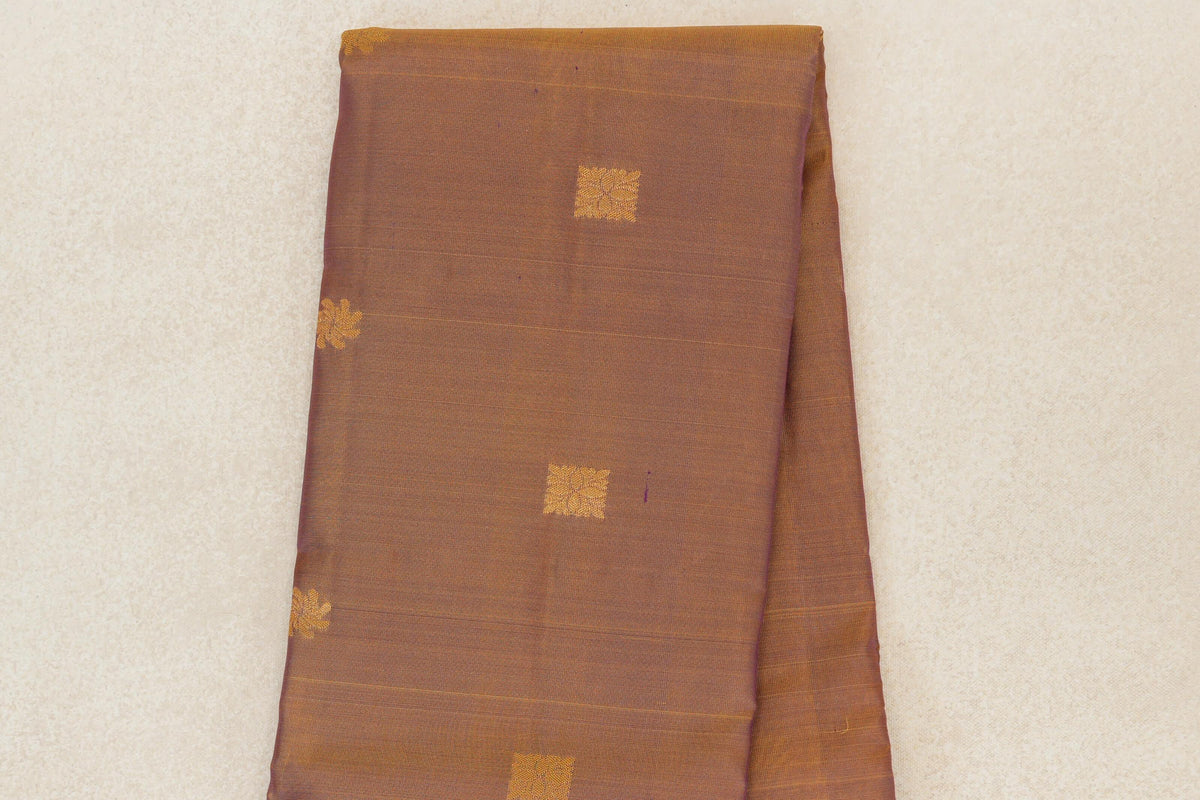 Folded Kanchipuram silk saree body in muted magenta and yellow, with small gold-colored square motifs and fine horizontal lines.