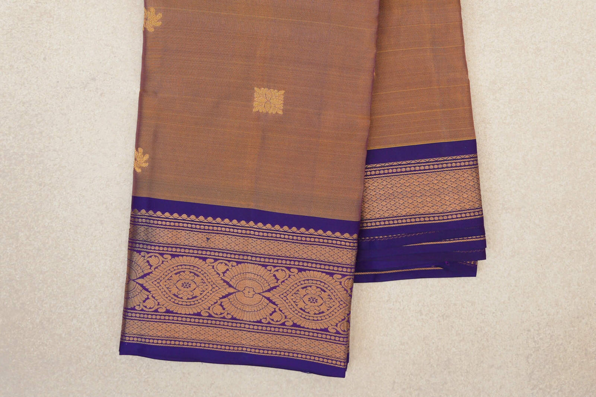 Folded light weight Kanchipuram silk saree with a magenta-yellow body, small gold motifs and a violet purple border of floral medallions and geometric bands.