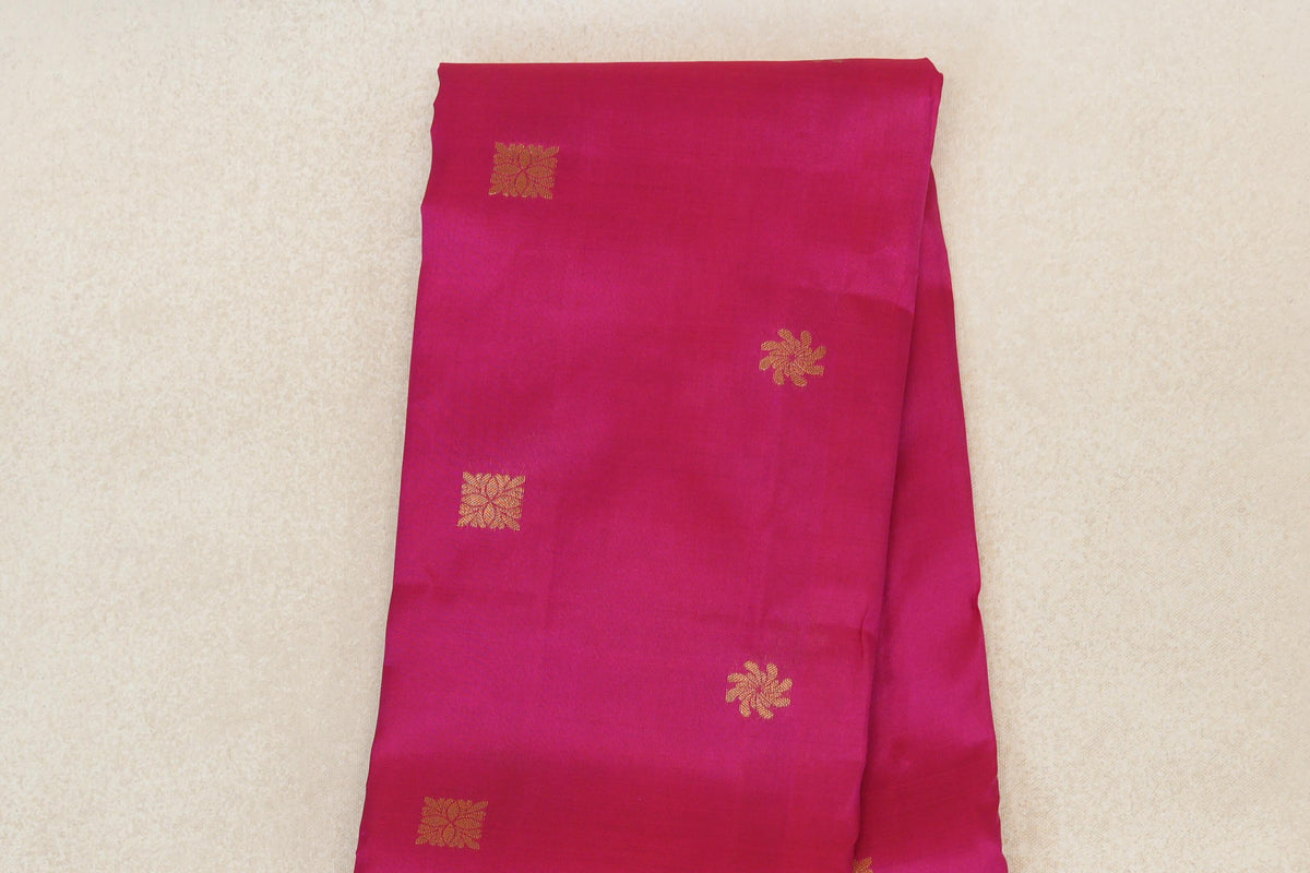Folded rani pink lightweight Kanchipuram silk saree body with scattered gold-toned square and floral motifs.