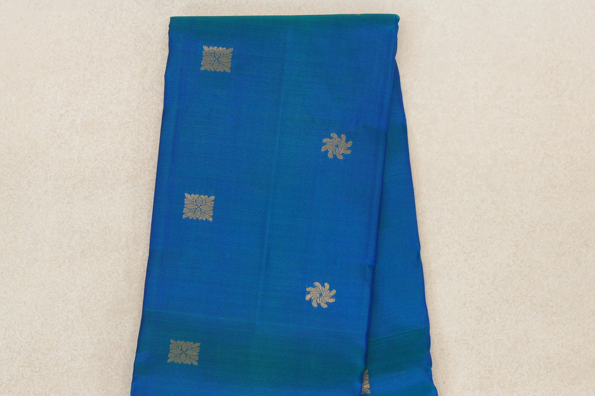 Folded peacock blue lightweight Kanchipuram silk saree with scattered gold-toned floral and square motifs and a deep royal blue edge.