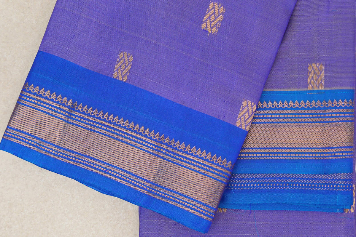 Close-up of a folded lavender Kanchipuram silk saree with scattered gold motifs and a royal blue border woven with gold patterned bands.