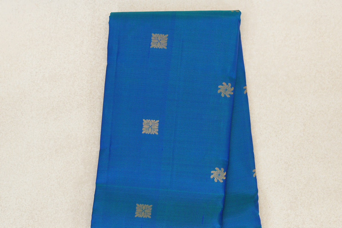 Folded peacock blue light weight Kanchipuram silk saree, showing spaced gold-toned floral motifs across the body.