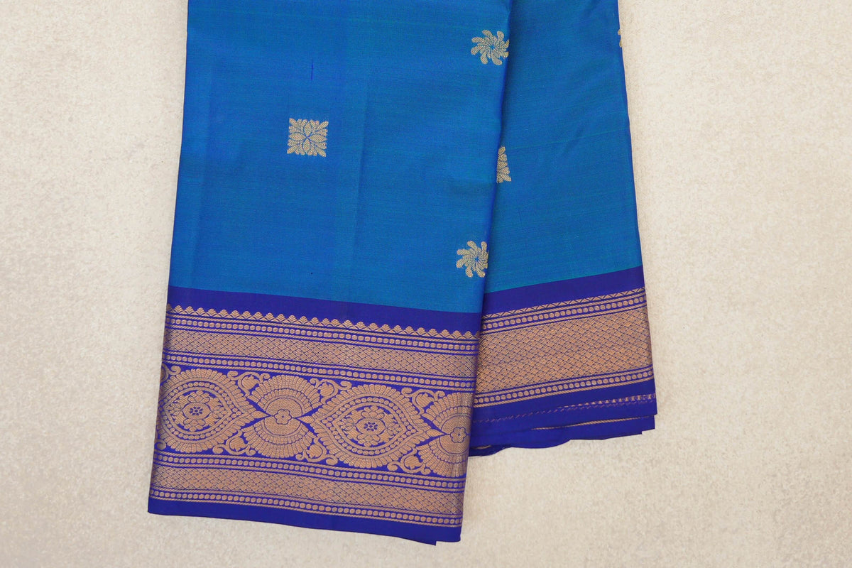 Folded peacock blue light weight Kanchipuram silk saree with scattered gold-toned motifs and an ornate deep royal blue border.