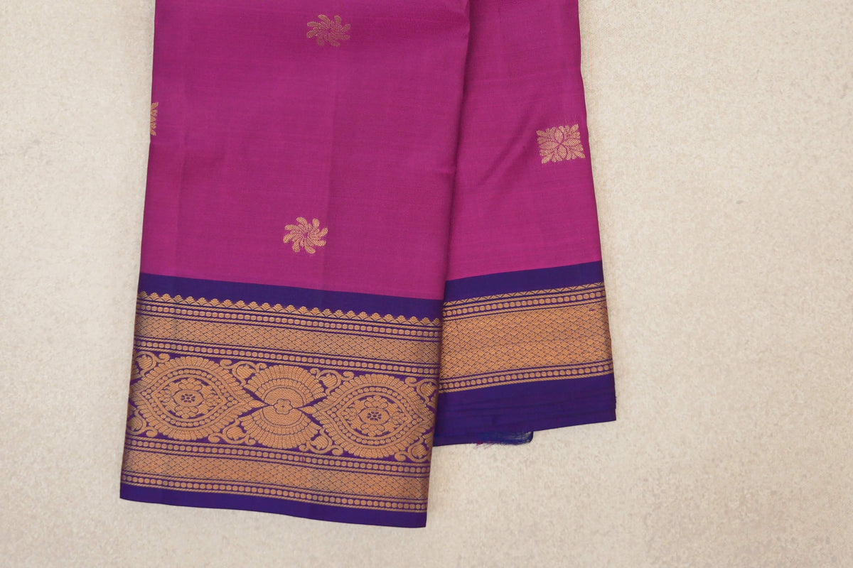Folded deep magenta lightweight Kanchipuram silk saree with scattered gold motifs and violet purple borders woven with gold patterns.