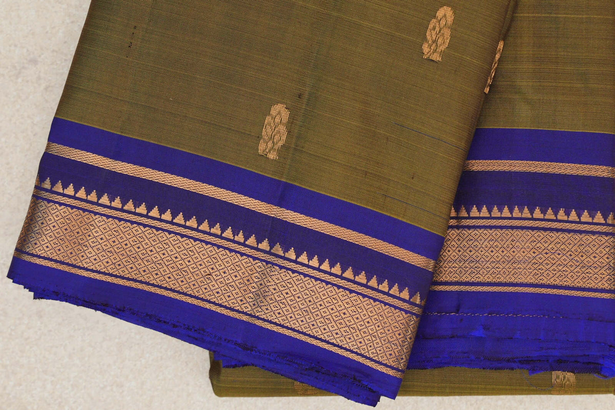 Folded lightweight Kanchipuram silk saree showing an olive green body with gold motifs and a deep royal blue border with gold geometric bands.
