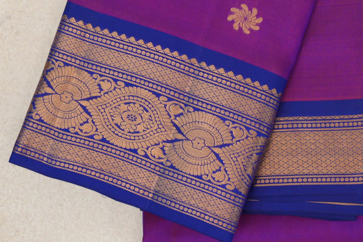 Folded light weight Kanchipuram silk saree showing a rani pink body with a gold motif and deep royal blue borders with ornate gold patterns.