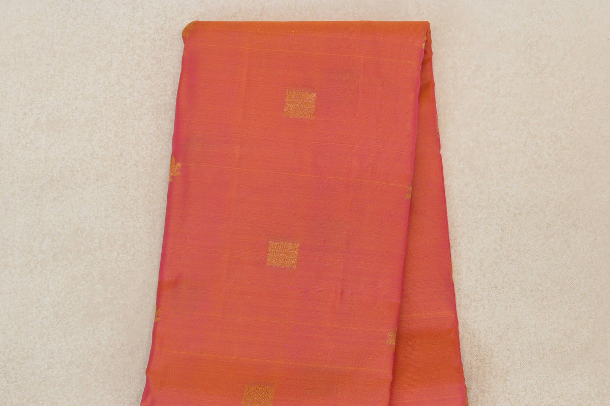 Folded Kanchipuram silk saree showing a warm pink and yellow body with spaced gold square motifs and subtle horizontal lines.