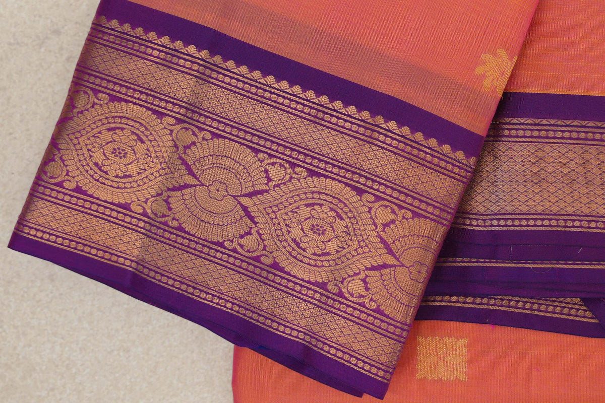 Folded light weight Kanchipuram silk saree showing a pink and yellow body and violet purple border with gold-toned floral medallions and lattice bands.